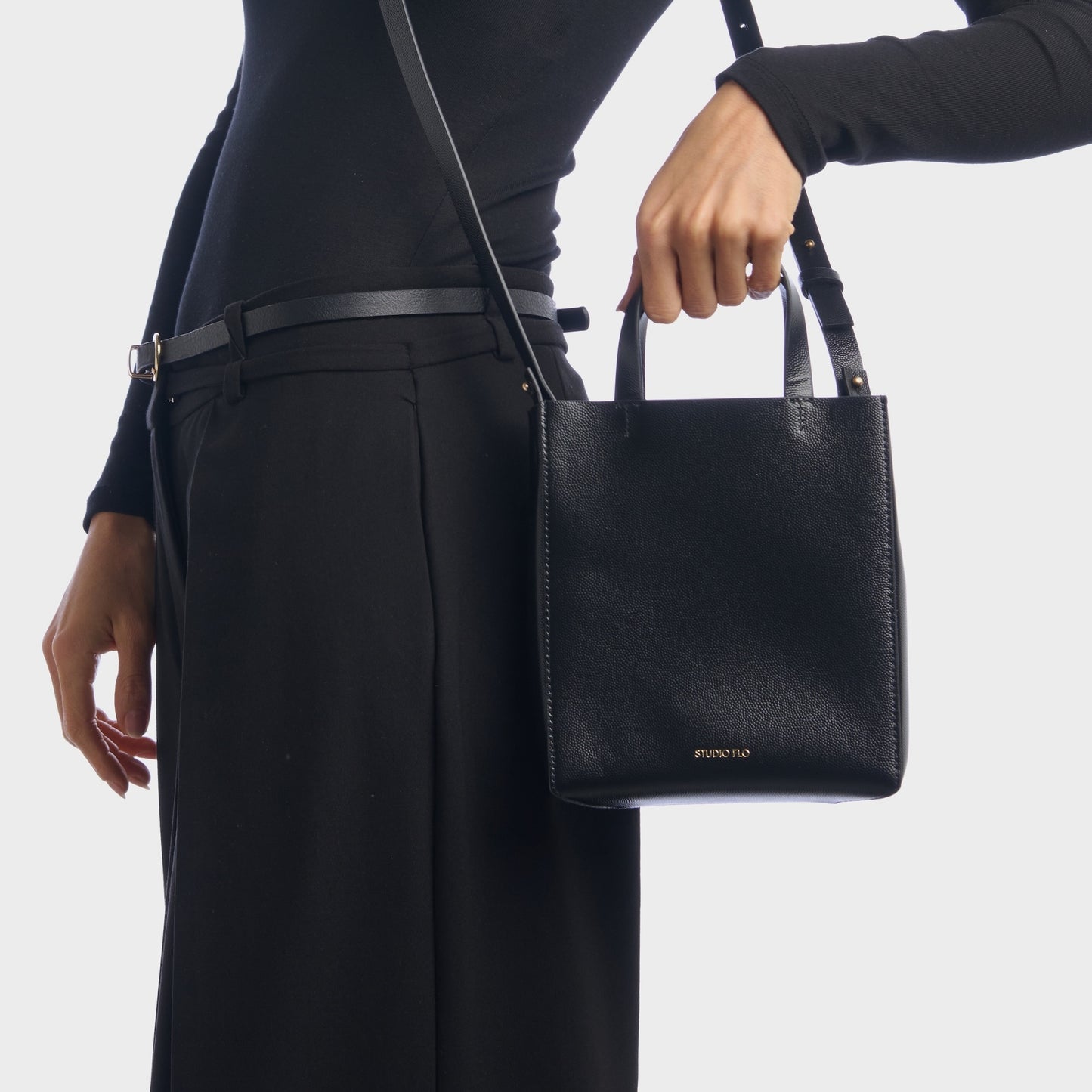 Elegant black mini handbag held by top handles, worn with suit