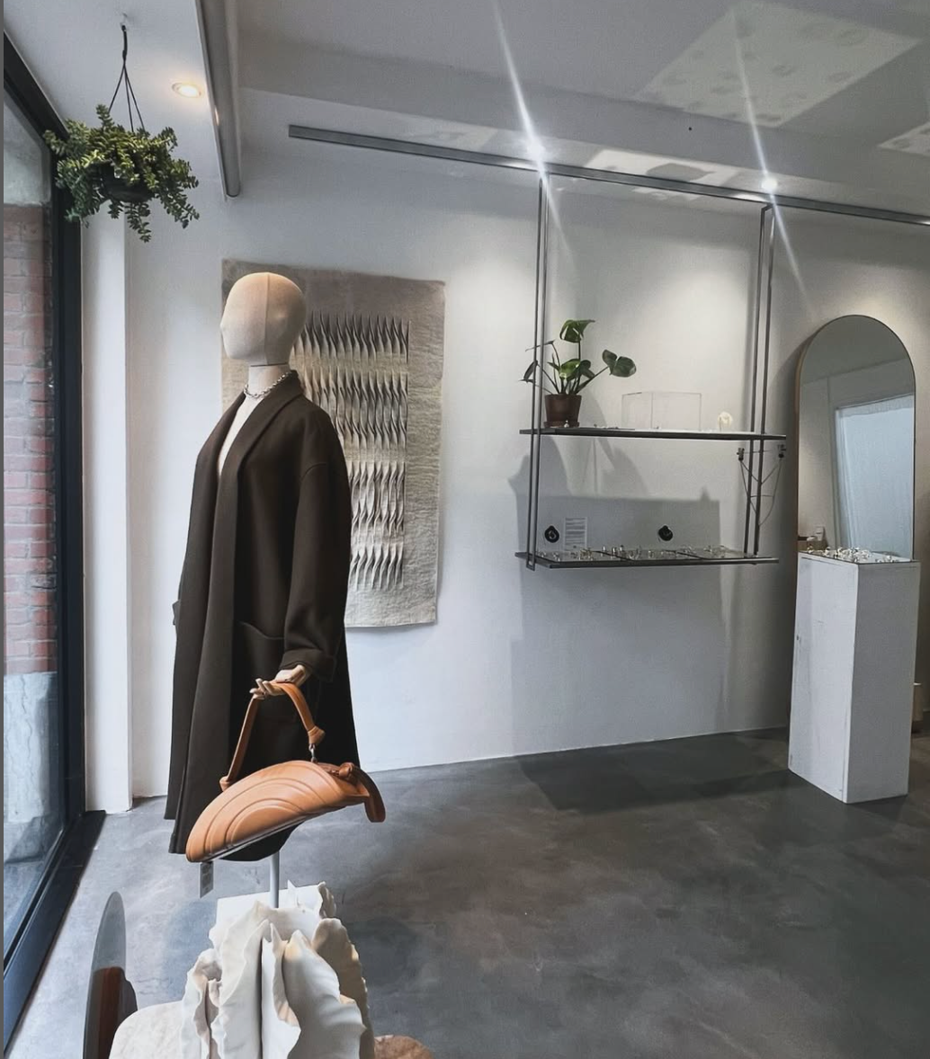 Mannequin wearing a coat and holding a handbag in a modern interior setting.