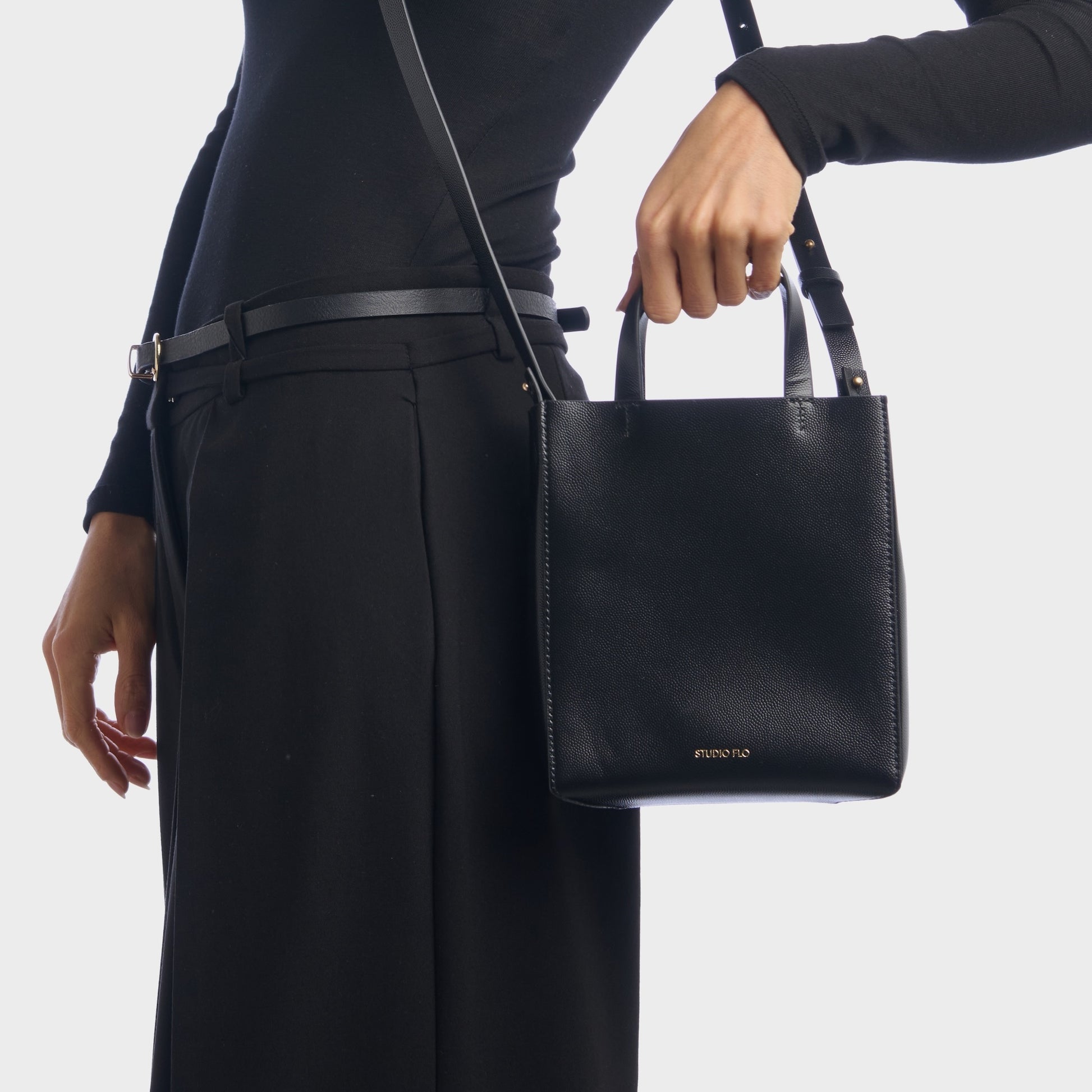 Elegant black mini handbag held by top handles, worn with suit