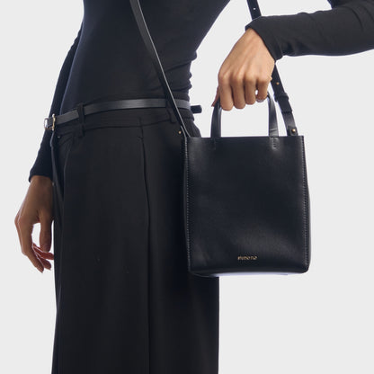 Elegant black mini handbag held by top handles, worn with suit